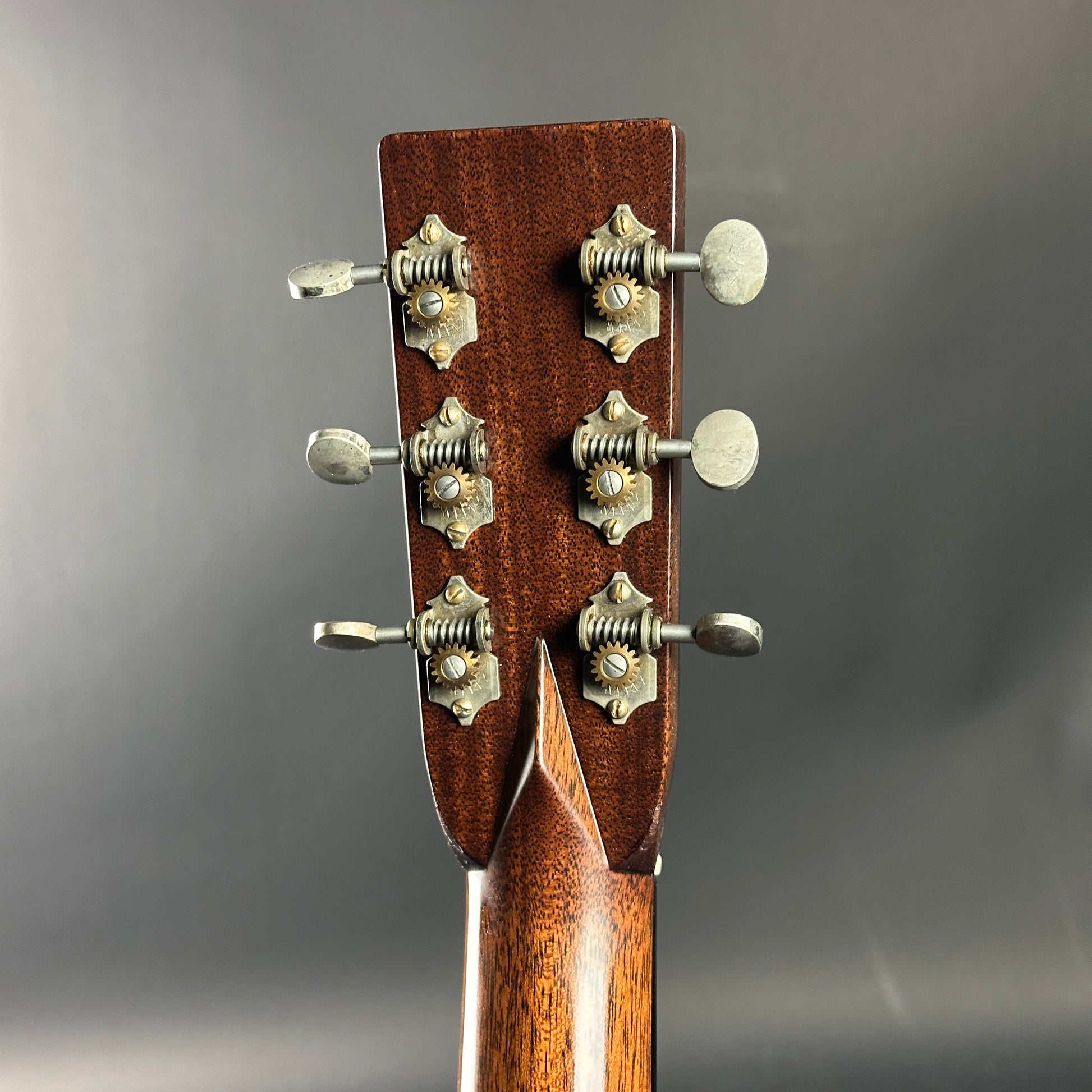 Close-up of a guitar headstock with tuning pegs on a gray background
