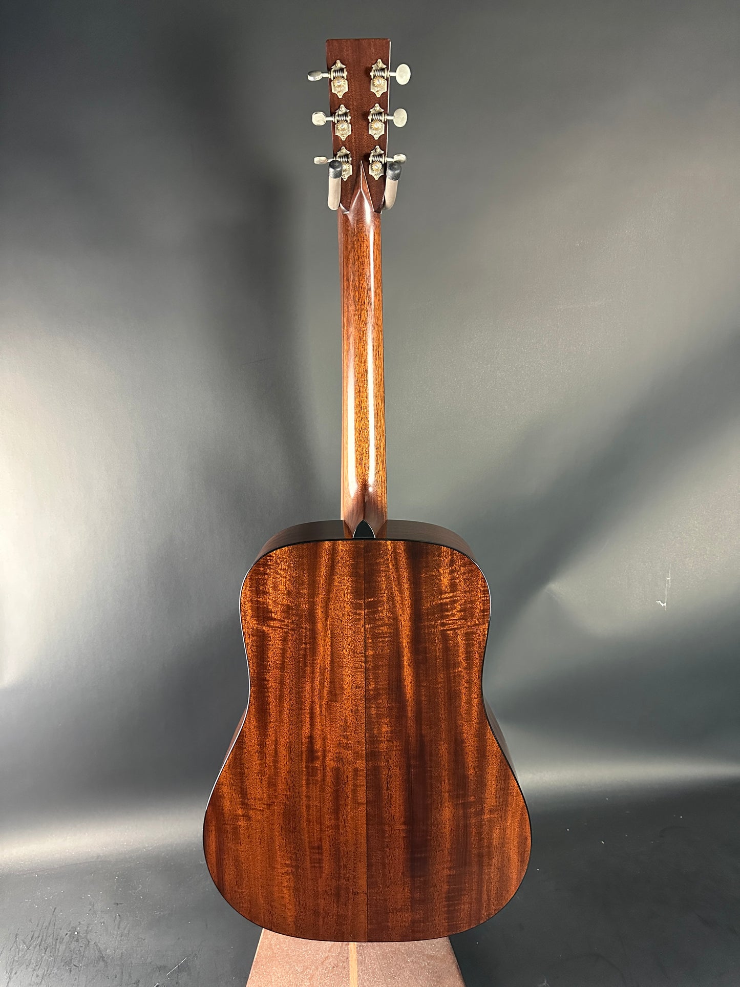 Top view of a wooden acoustic guitar on a reflective gray surface
