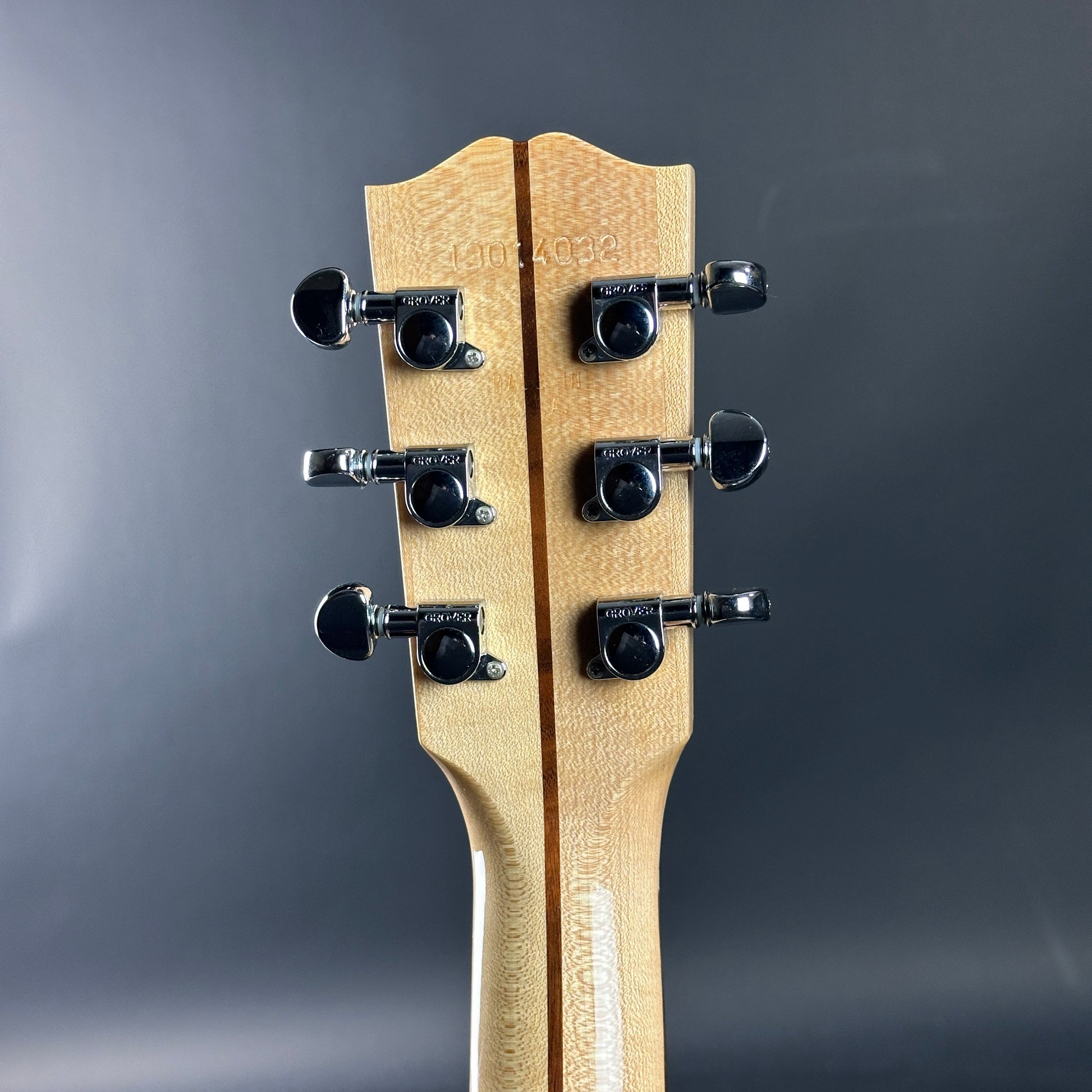 Close-up of a guitar headstock with tuning pegs on a dark gray background