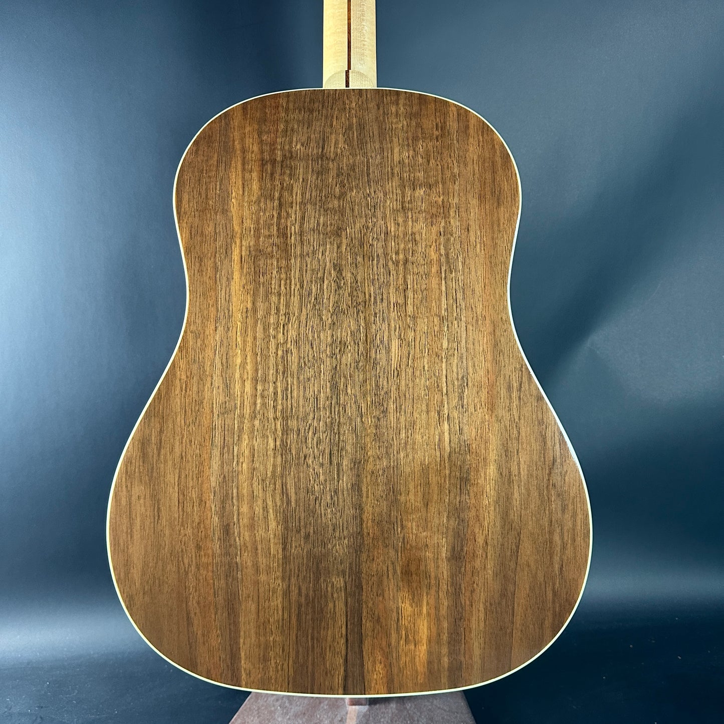 Back view of a wooden acoustic guitar against a blue background