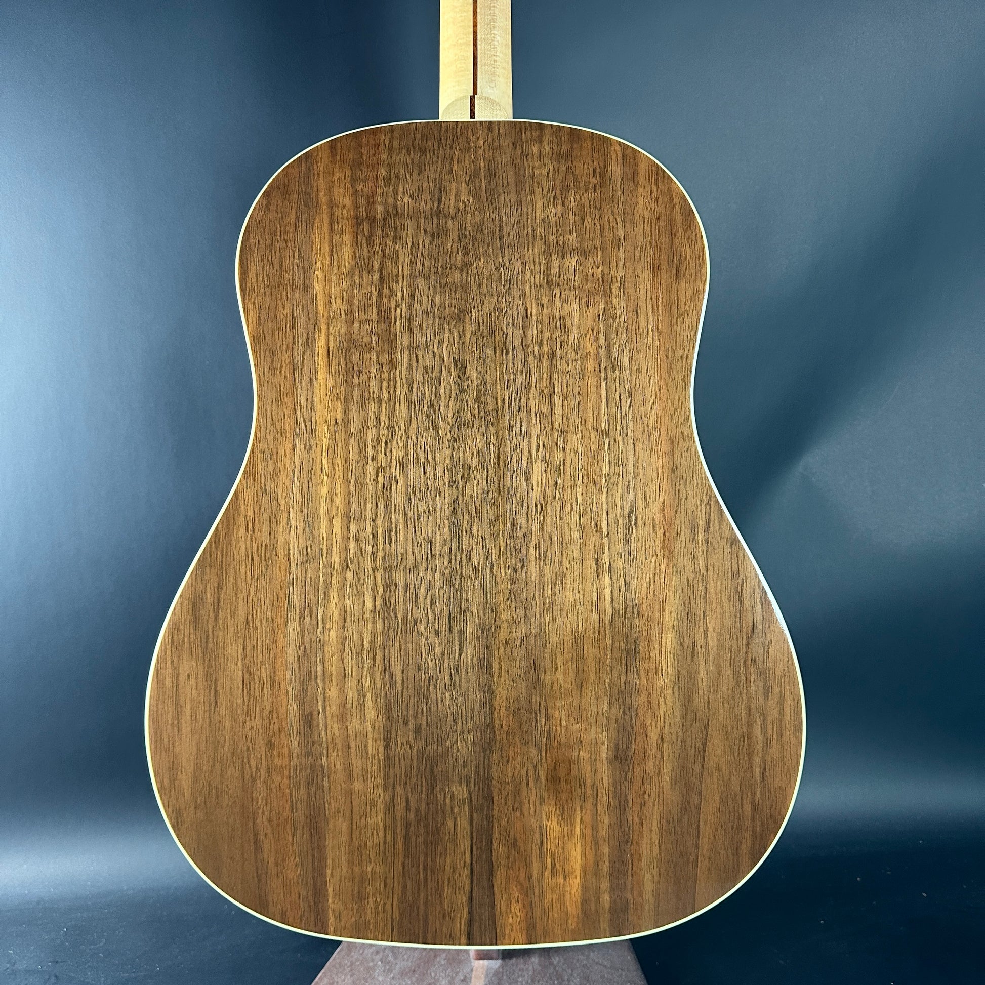 Back view of a wooden acoustic guitar against a blue background