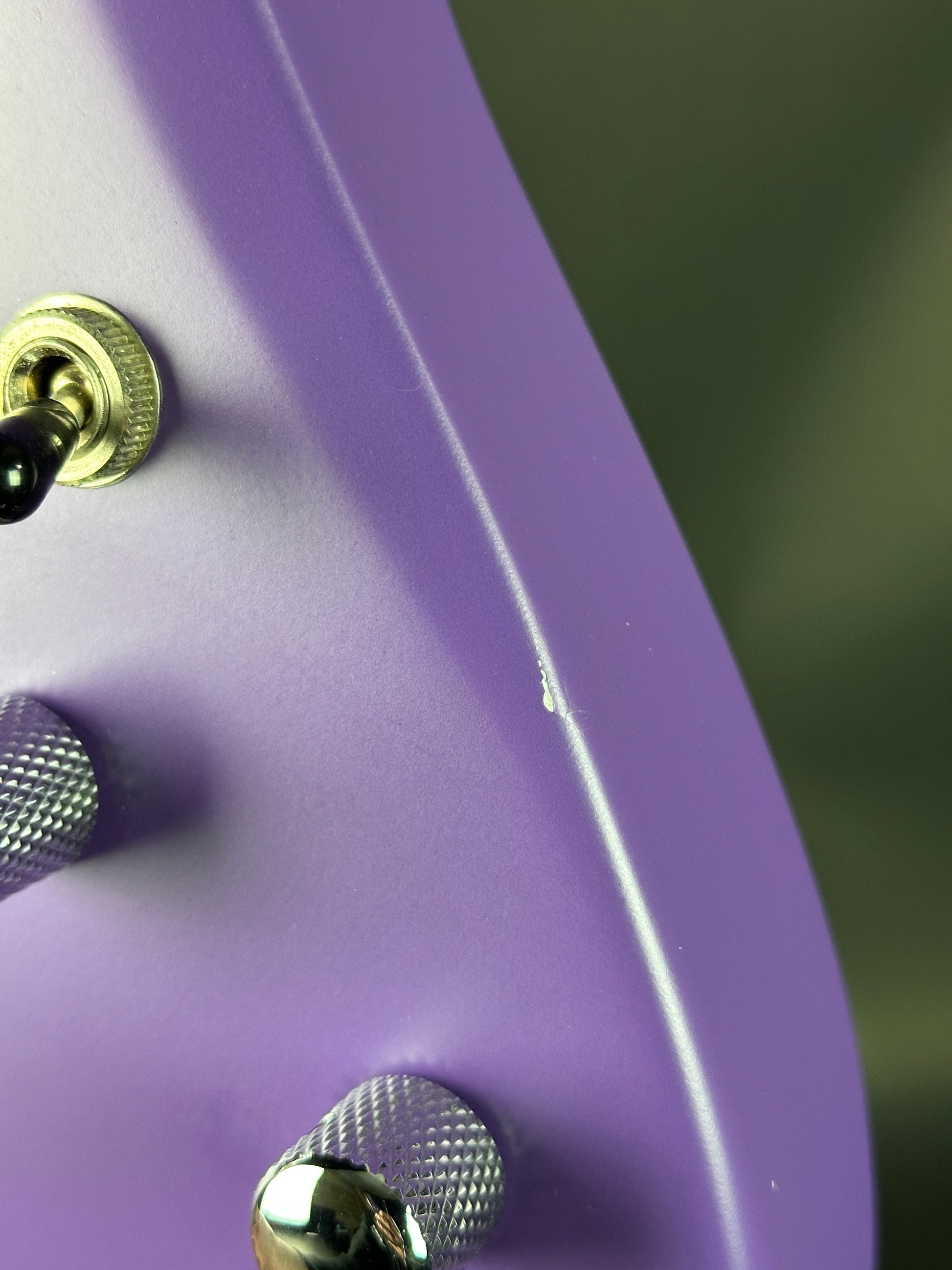 Close-up of a purple electronic device with gold knobs and a blurred background