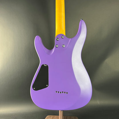 Purple electric guitar with a wooden neck on a stand against a dark background