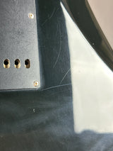 Close-up of a glossy black guitar body or body panel with visible scratches, screw holes, and a light-colored surface reflected in the upper section.