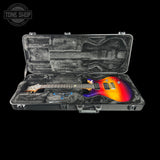 An electric guitar with a vibrant sunset gradient finish (orange, yellow, red, purple) resting inside its open black hard case on a solid black background. A Tone Shop logo is visible in the top-left corner.