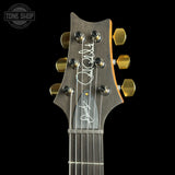Close-up of the headstock of an electric guitar against a black background, featuring a dark wood finish, gold tuning pegs, and white signatures of Jim Phillips and David Gilmour on the backplate.