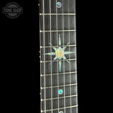 Close-up of a guitar neck fretboard with a dark wood finish, metal frets, and iridescent inlay dots including a compass-style motif in the center. A Tone Shop watermark is visible in the upper left corner.