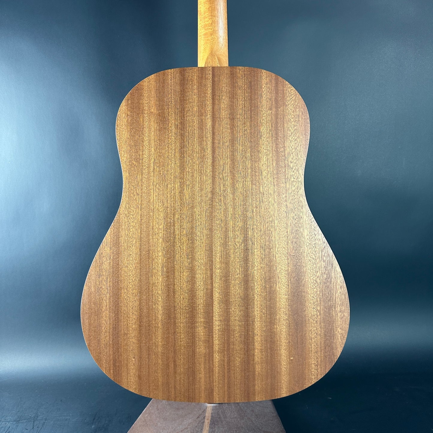 Back view of a wooden acoustic guitar against a blue gradient background