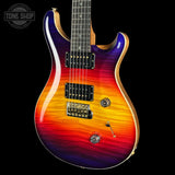 A double-cutaway electric guitar with a vibrant sunburst finish transitioning from purple and blue at the top to orange and red at the bottom, shown against a solid black background.