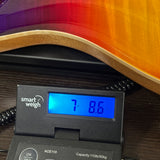 A close-up of a digital smart weigh scale displaying 7.86 lbs, positioned under the edge of a guitar with a vibrant orange and yellow sunburst finish.