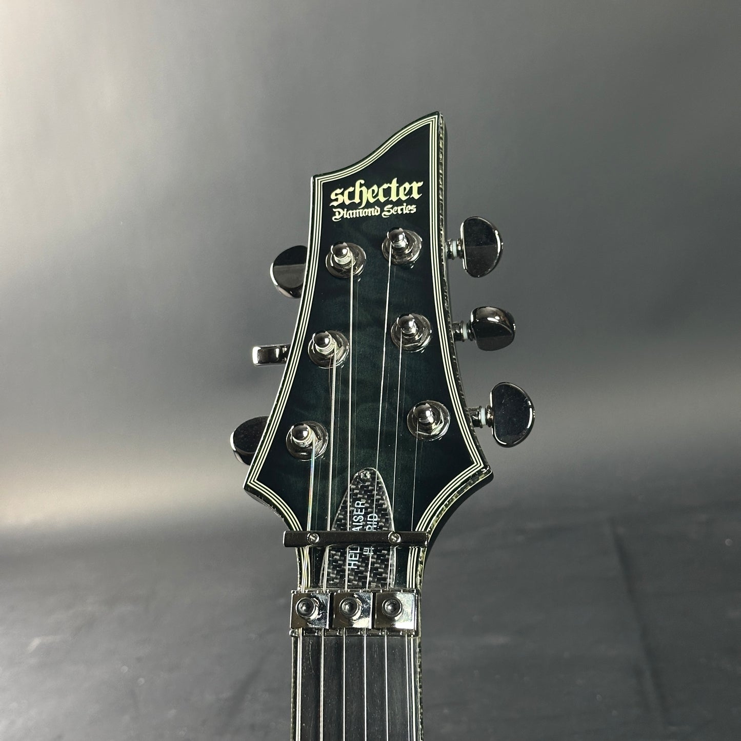 Guitar headstock with 'Schecter' branding on a gray background