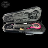 A pink and red electric guitar inside an open black hard case with gray foam padding, photographed against a black background. A Tone Shop watermark is visible in the top-left corner.