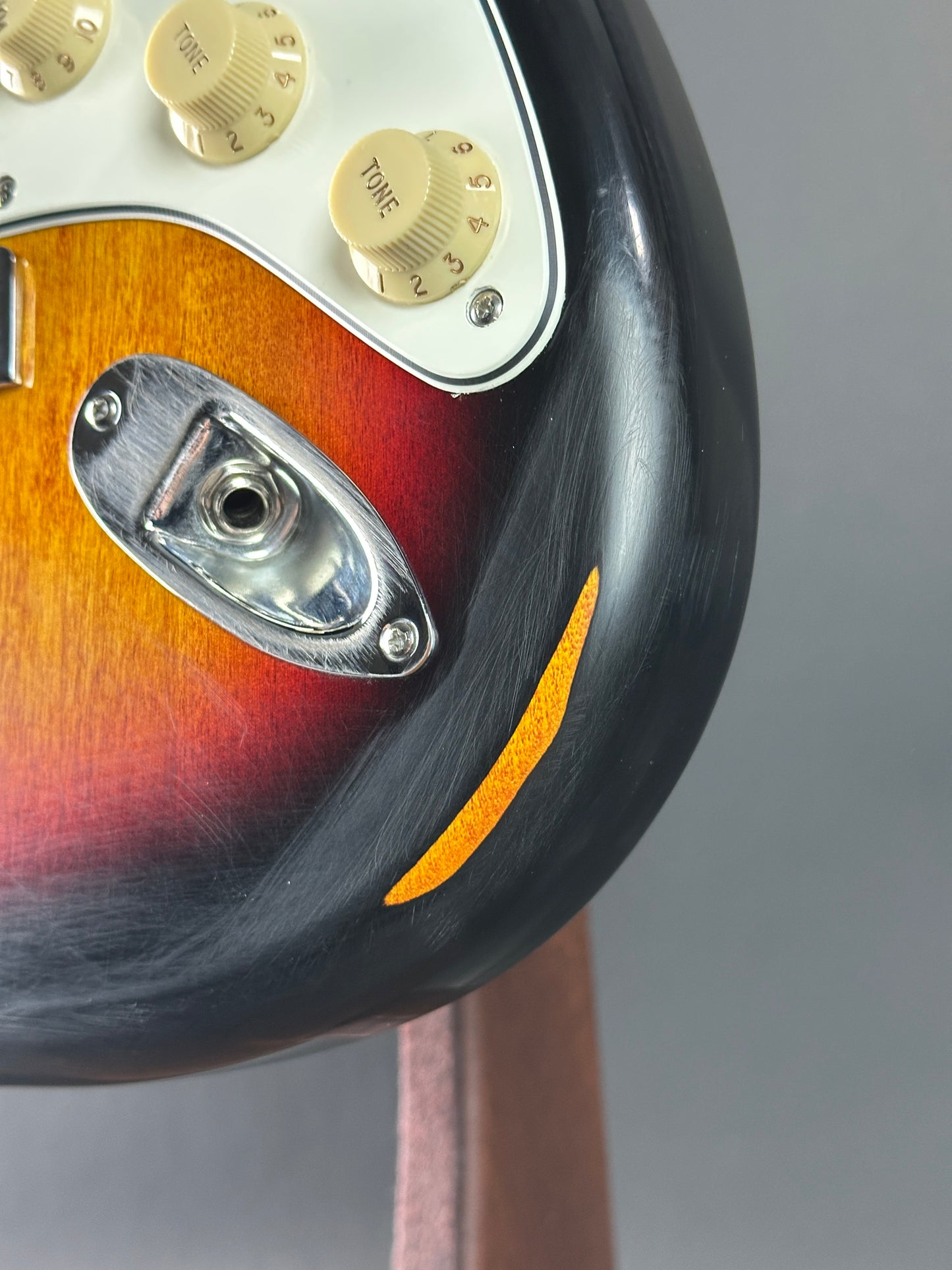 Close-up of a guitar's headstock with tuning pegs and brand name on a gray background