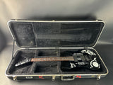Black electric guitar in a hard-shell case on a gray background