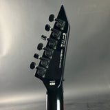 Close-up of a black electric guitar headstock with tuning pegs on a reflective gray background