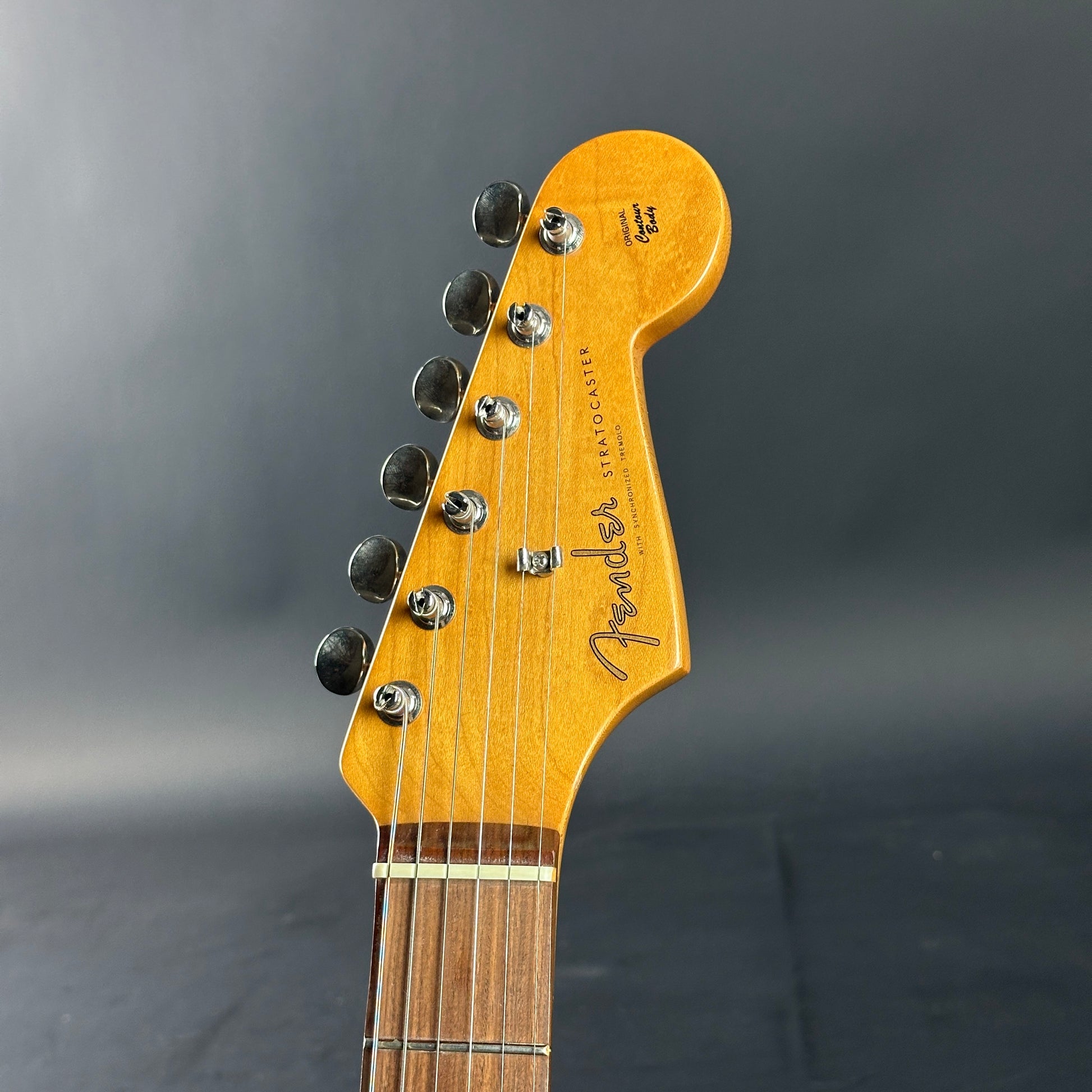 Guitar headstock with Fender logo on a gray background
