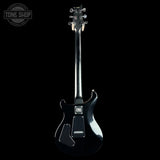 A black electric guitar shown from the back against a solid black background, with a Tone Shop watermark in the upper left corner.