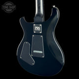 The rear view of a glossy black PRS Custom electric guitar body, featuring a silver PRS logo plate and a black pickguard, set against a solid black background.