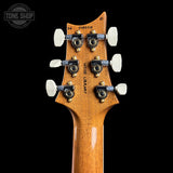 Close-up of the headstock of a wooden guitar, showing six tuning pegs, white tuning keys, and the text 'WOOD LIBRARY' and 'TONE SHOP' on a black background.