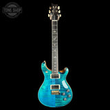 A blue and turquoise flamed maple top electric guitar with gold hardware, shown against a solid black background. A Tone Shop watermark is visible in the top-left corner.