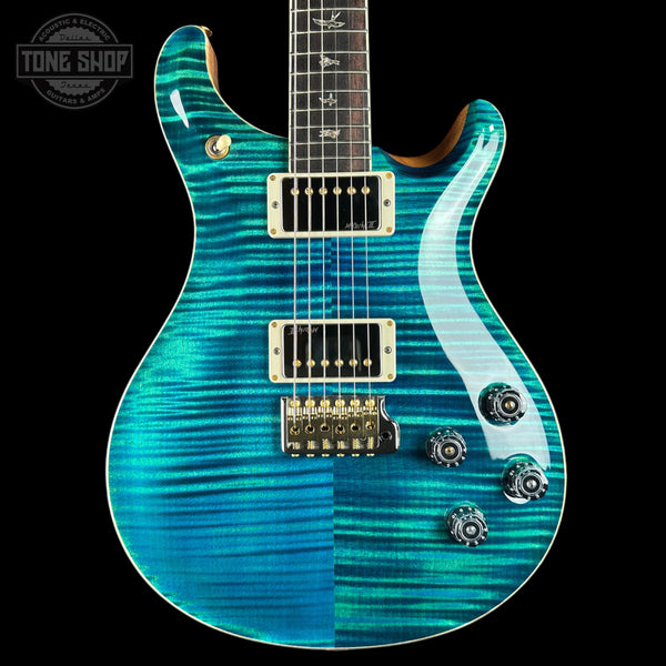 A double-cutaway electric guitar with a vibrant turquoise and teal flamed maple top, featuring gold hardware and a dark fretboard, shown against a solid black background.