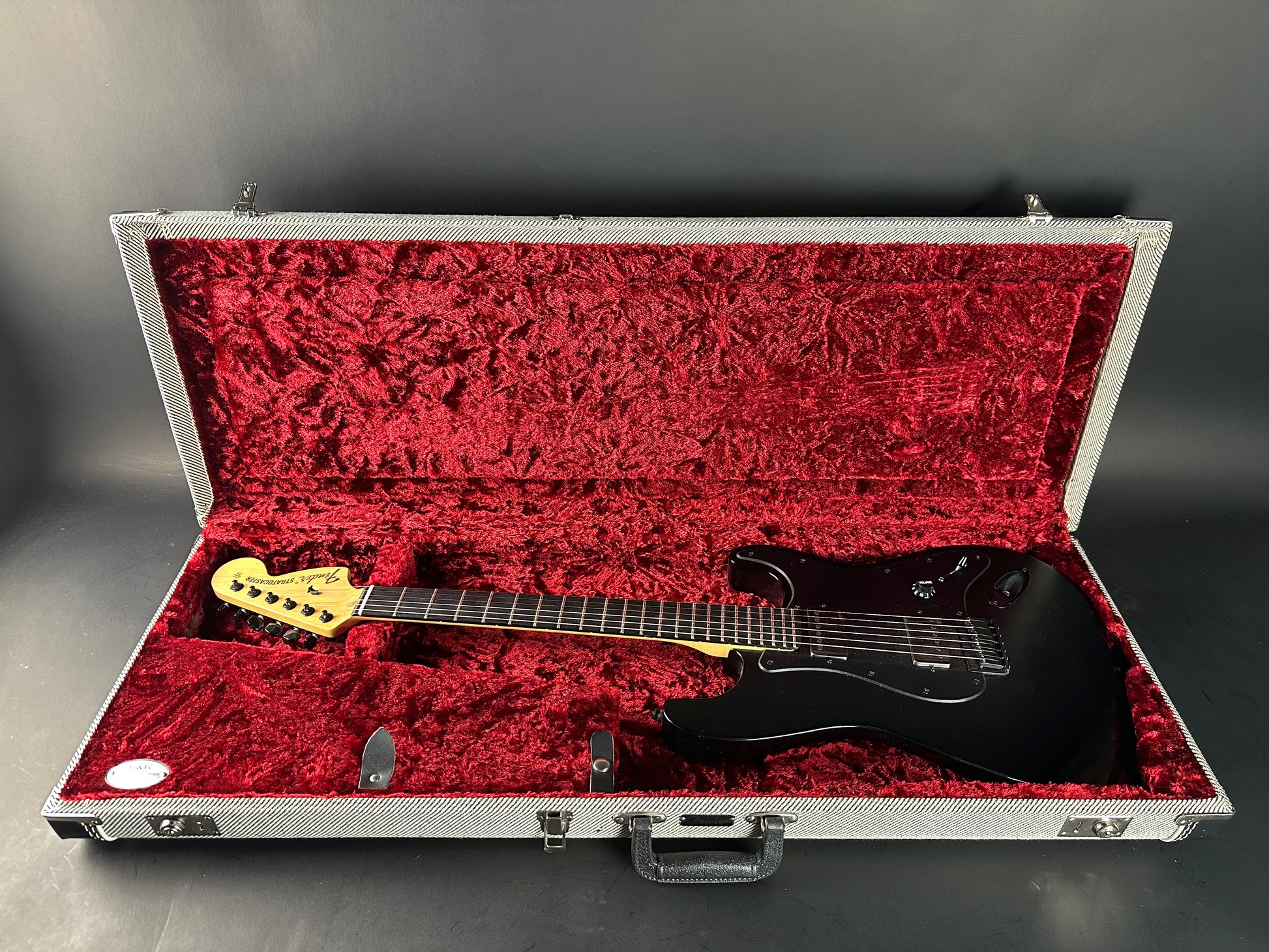 Black electric guitar with yellow pickguard in a red-lined case on a gray background