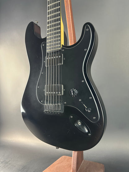Black electric guitar with wooden neck and fretboard on a gray background