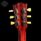 Close-up of the headstock of an electric guitar against a black background, showing six tuning pegs with yellow grips and a red glossy finish. A Tone Shop watermark is visible in the top left corner.