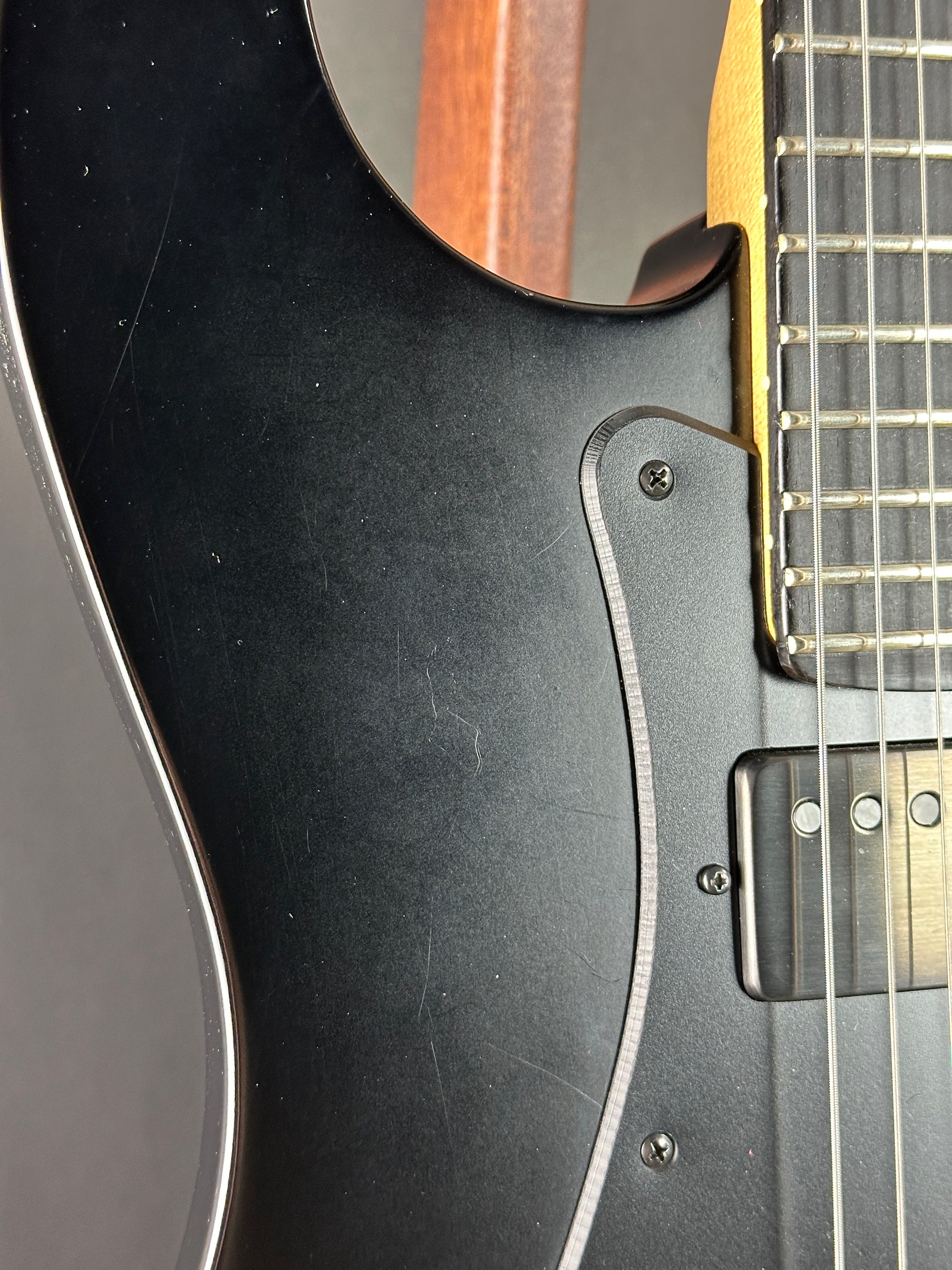 Close-up of a black electric guitar with a visible pickguard and part of the neck.