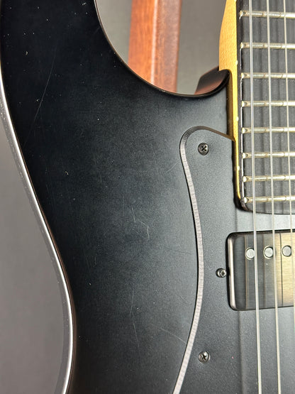 Close-up of a black electric guitar with a visible pickguard and part of the neck.