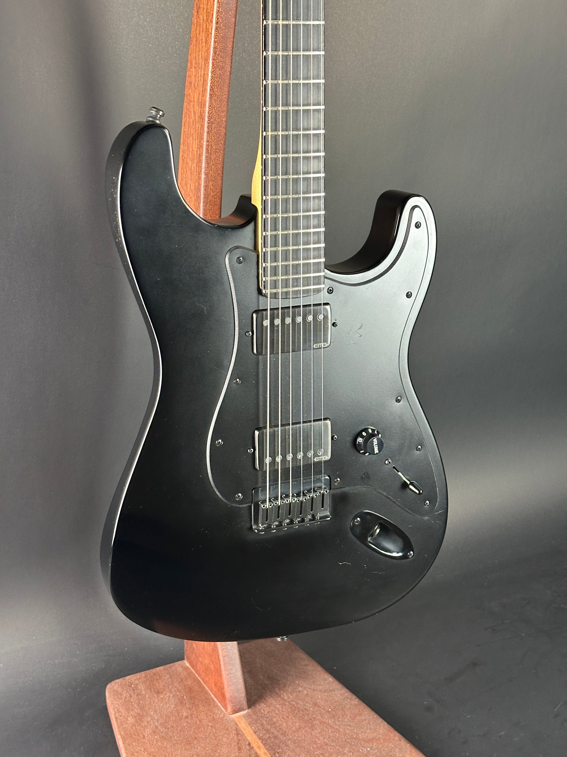 Black electric guitar with a wooden fretboard on a dark background