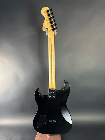 Black electric guitar with wooden neck on a gray background
