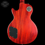 The back of a Gibson electric guitar with a vibrant red cherry wood finish, featuring a black pickguard and a silver chrome output jack, shown against a solid black background.