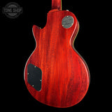 The back of a Gibson electric guitar with a vibrant red cherry wood finish, featuring a black pickguard and a silver circular plate, shown against a solid black background.