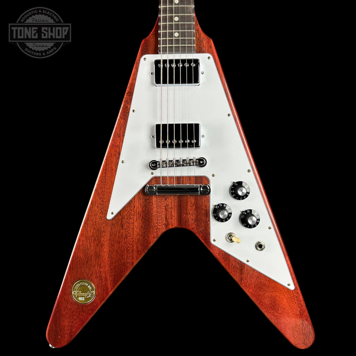 A classic electric guitar with a distinctive V-shaped body, featuring a reddish-brown wood finish and a white pickguard. The guitar is shown from a front-facing angle against a solid black background, with a 'TONE SHOP' watermark in the upper left corner.
