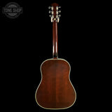 The back view of a brown acoustic guitar with a glossy finish, set against a solid black background. A Tone Shop watermark is visible in the top left corner.