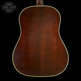 The back of an acoustic guitar with a rich reddish-brown wood finish and a thin cream-colored edge trim, shown against a solid black background with a Tone Shop watermark in the top left corner.