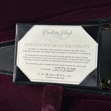 A black leather guitar case opened to reveal a Certificate of Authenticity insert from Custom Shop Martin. The insert features a cream-colored paper label with black text, and the case is set against a dark burgundy velvet background.