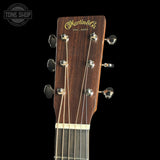 Close-up of a Martin & Co acoustic guitar headstock, showing the dark brown wood grain, gold script logo, and six silver tuning pegs against a solid black background.