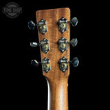Close-up of the headstock of an acoustic guitar, showing six black and gold Fazzio tuning pegs on a brown wood grain background, set against a solid black backdrop.