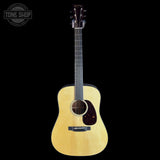 A natural wood acoustic guitar with a dark headstock, shown vertically against a solid black background. A circular 'TONE SHOP' watermark is visible in the top-left corner.