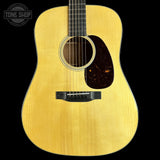 A close-up studio shot of an acoustic guitar's front body, showing a natural wood finish, sound hole, pickguard, and bridge against a solid black background. A Tone Shop watermark is visible in the top-left corner.