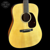 A close-up studio shot of an acoustic guitar body against a black background, showing a natural wood finish, sound hole, pickguard, and bridge. A Tone Shop watermark is visible in the upper left corner.