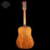 The back of a wooden acoustic guitar, showing the rich grain of the mahogany body and neck, with six silver tuning pegs on the headstock, set against a solid black background. A 'TONE SHOP' watermark is visible in the top left corner.