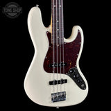 A white electric bass guitar with a dark reddish-brown tortoiseshell pickguard, shown against a solid black background. A Tone Shop watermark is visible in the top-left corner.