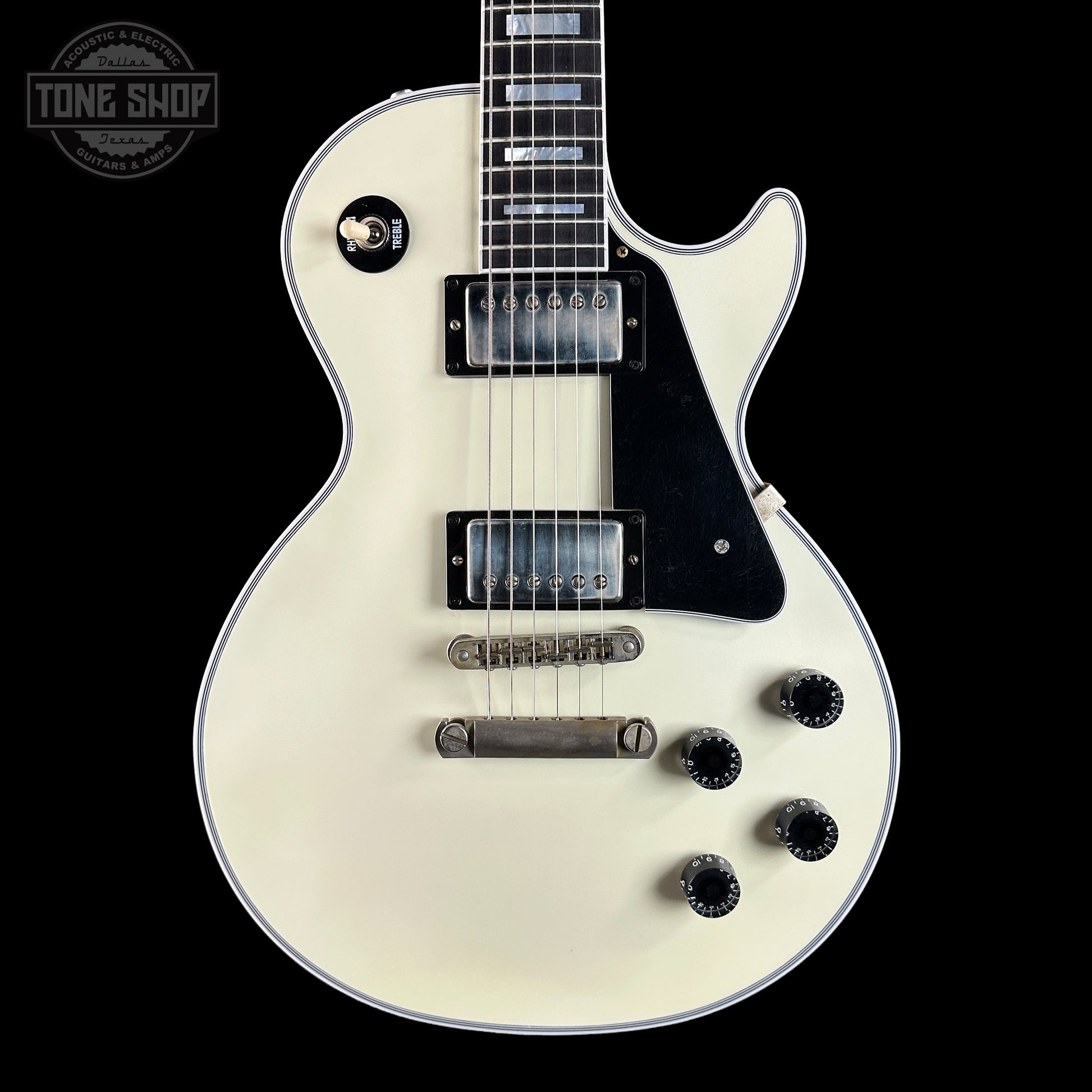 White electric guitar with black details on a black background, featuring the Tone Shop logo.