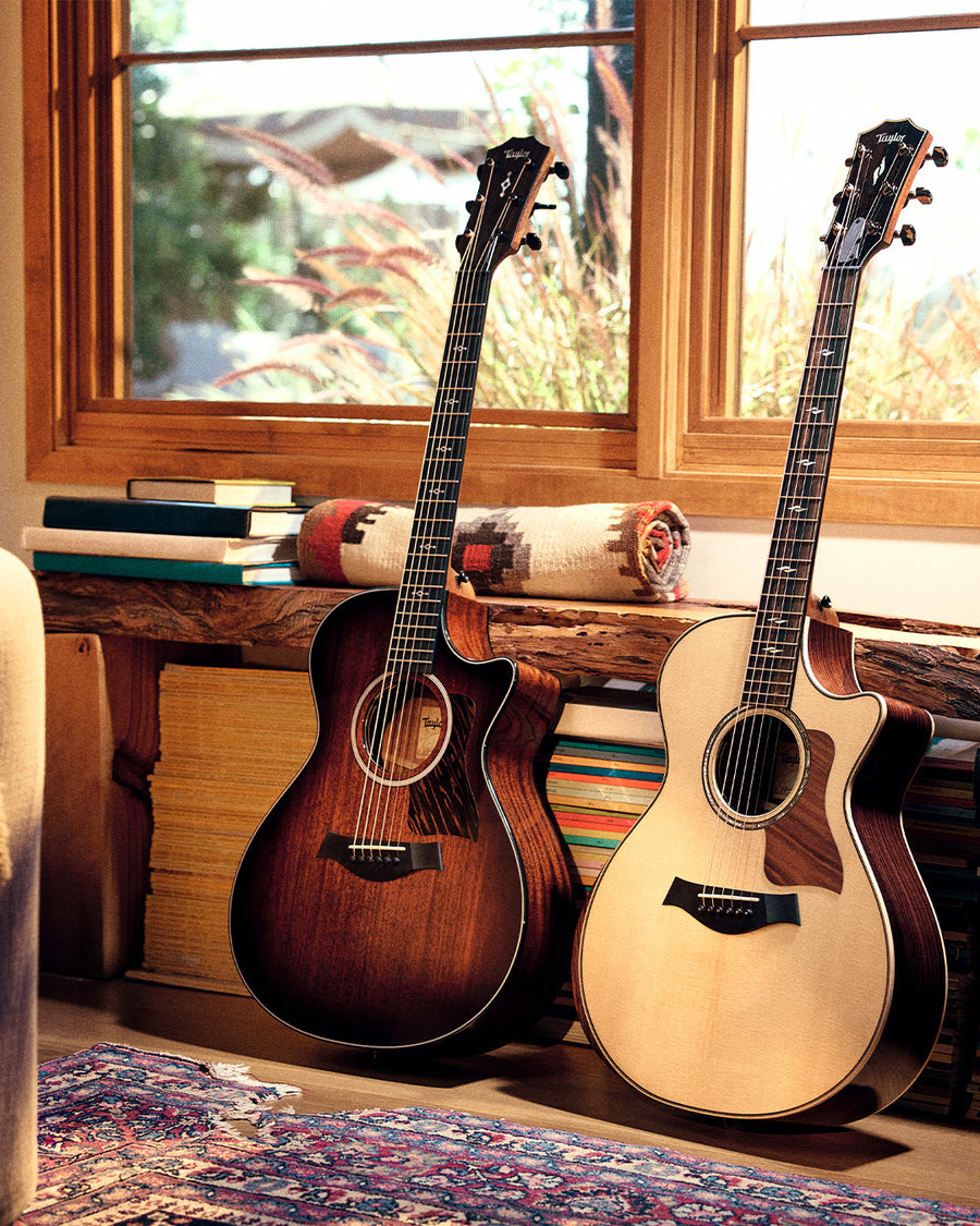 Two taylor acoustic guitars leaning against a shelf in natural light.