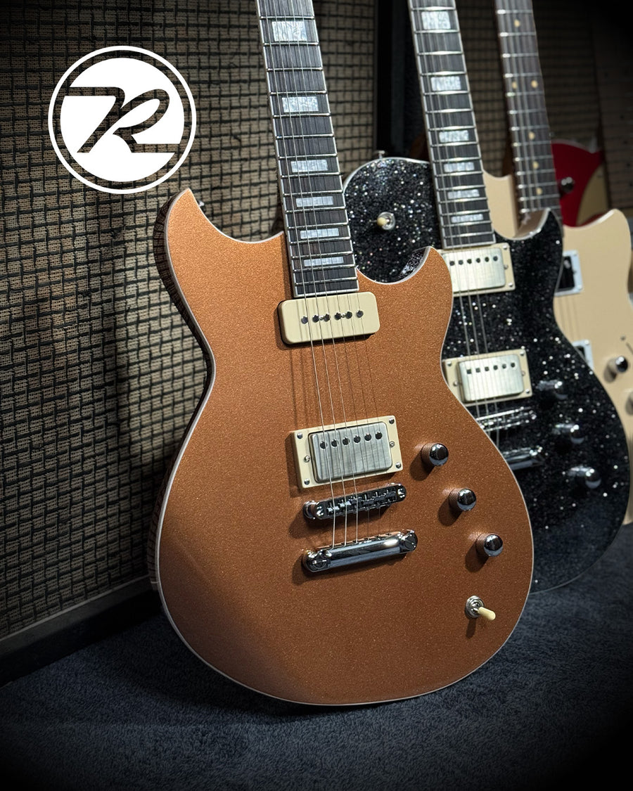 A group of reverend guitars against a basketweave amp cabinet.