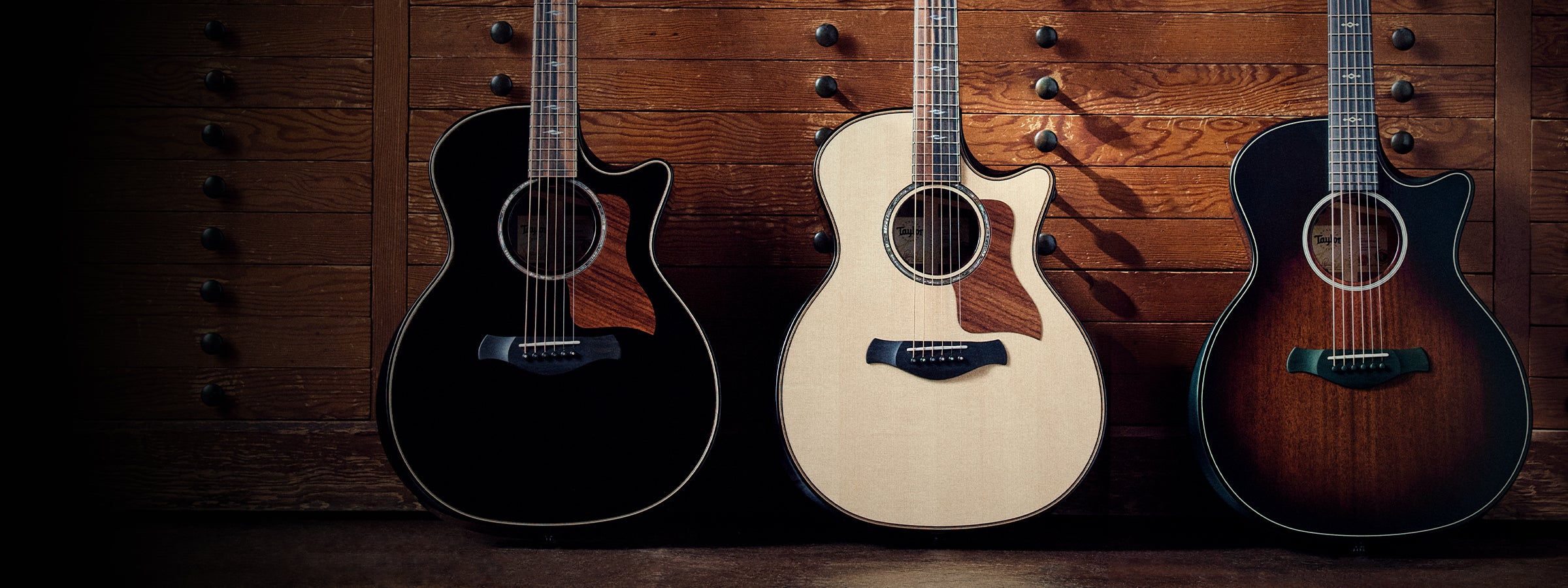Three Taylor guitars against a wooden background