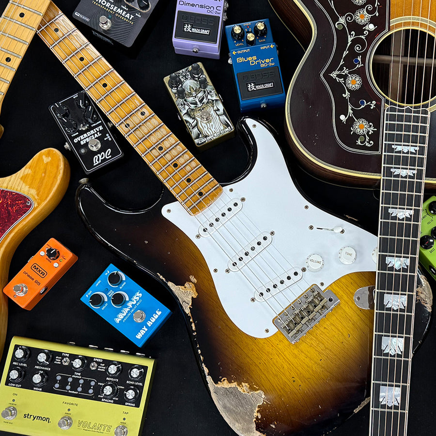 A group of guitars and pedals on a black background.